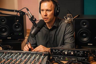 Cucu Repping achter een audiomengtafel in de podcaststudio met koptelefoon en studiomonitors